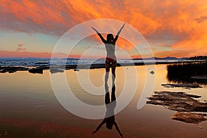 Silhouette of young woman standing on the beach at the sunset