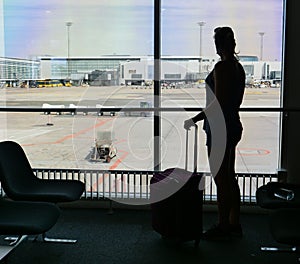 SILHOUETTE: Young woman stands by the window and looks at the airport runway.