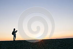 Silhouette of a young woman taking pictures on the camera at sunset