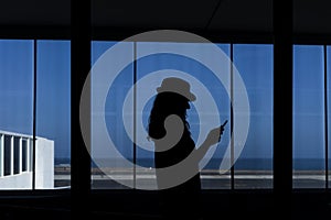 Silhouette of a young woman using mobile phone in the airport. Travel concept