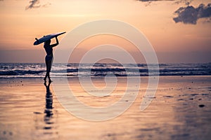 Silhouette of young woman walking along the beach at sunset