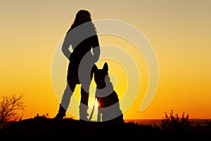 Silhouette of young woman walking with a dog in the field at sunset, pet sitting near girl`s leg on nature,couple of friends huma