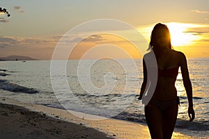 Silhouette of young woman walking by the sea at sunset