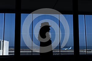 Silhouette of a young woman watching an airplane taking off in the airport through a window. Travel concept