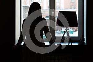 Silhouette of a young woman at the window. Vintage lamp on the windowsill