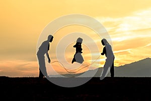 Silhouetted children rope skipping in sunset