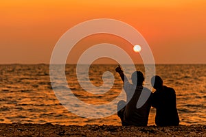 Silhouetted couple sitting, and relax on beach in love and embrace, sunset in the beach.