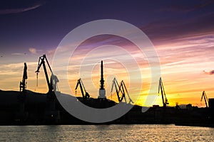 Silhouetted cranes at shipyard,