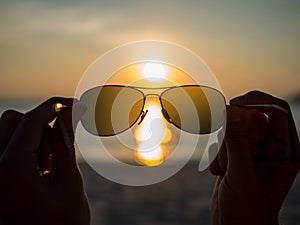 Silhouetted of eye glasses with hands holding, with sunset at beach view