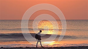 Silhouetted figure walking along seashore with