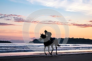 A silhouetted horse rider galloping across a beach at sunrise