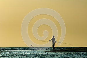 A silhouetted man fishes at sunset along Barefoot Beach, Florida