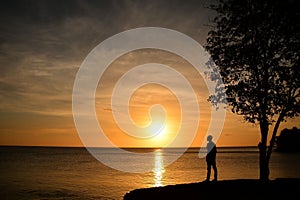 Silhouetted man stands on a beach at sunset, looking out over the horizon with a peaceful expression