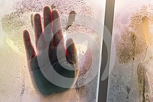 Silhouetted palm of hand, behind the window, selective focus on drop water and surface on glass.