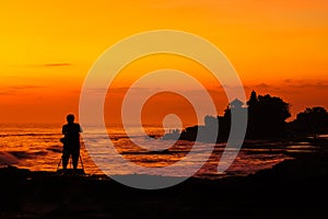 Silhouetted of photographer and Tanah Lot at sunset, Bali, Indonesia.
