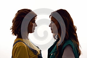 Silhouetted portrait of two young girls, twin sisters in casual wear looking at each other, posing together, standing