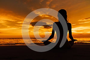 Silhouetted woman in lotus pose on background beautiful sunset on sea