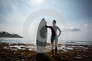 Silhouetted young woman surfer girl with white surfboard