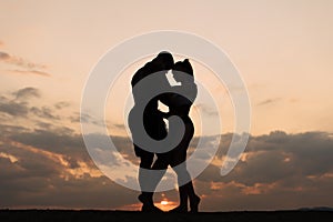 Silhouettes of athletic couple dancing on sunset. Beautiful cloudy sky background