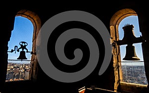 Silhouettes backlit by the evening sun of two restored bronze bells of the Torre de la Clerecia with views of the city of