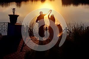 Silhouettes of the bride and groom, a man and a woman dancing near the river at sunset