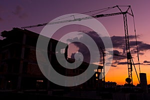 Silhouettes of building cranes at construction site. Real estate buildings at sunset