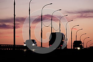 Silhouettes of cars and vans in front of sunset sky with silhouettes of streetlamps