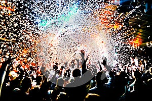 Silhouettes of concert crowd in front of bright stage lights with confetti