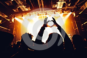 silhouettes of concert crowd in front of bright stage lights. People showing heart symbol. hands of audience making heart shaped h