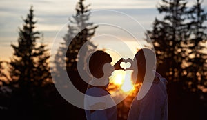 Silhouettes of couple in love at sunset gesturing heart