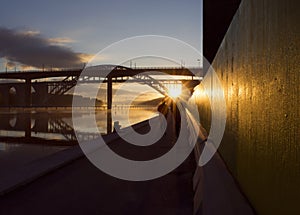 Silhouettes of couple running at beautiful, early dawn under a bridge.