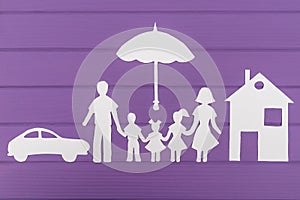 The silhouettes cut out of paper of man and woman with two girls and boy under the umbrella, house and car near