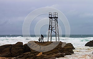 Silhouettes of daughter and parent on rocks by lifeguard tower looking out to stormy sea