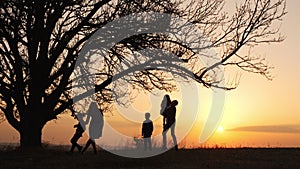 Silhouettes of family holding the hands and running in the meadow during sunset.