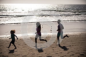 Silhouettes of family jogging along sea beach at sunrise. Outdoor workout, silhouettes of runners, sport and healthy