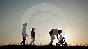 Silhouettes family is together at sunset. Young boy learning to ride bicycle, father teach his son to ride a bike in the