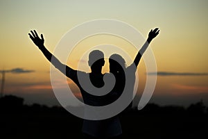 Silhouettes of father and daughter on his shoulders with hands up having fun, against sunset sky.