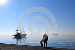 Silhouettes of father and son in front of Thermaikos Gulf, Thessaloniki Greece. Blue sea and sailing boat in the mist