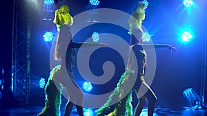 Silhouettes of female dancers in revealing carnival costumes and headdresses with feathers dancing in a dark studio with