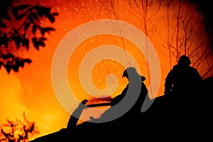 Silhouettes of firemen on a roof of a burning house