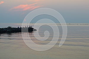 Silhouettes of fishermen on breakwater at sunrise