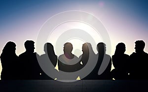 Silhouettes of friends sitting on stairs over sun