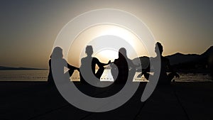 Silhouettes of girls sitting in yoga lotus pose at sunset on sea pier