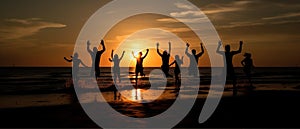 Silhouettes of a group of people on the beach, joyfully jumping up against the backdrop of the setting sun. The scene is