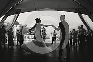 Silhouettes of happy bride and groom gently dancing at wedding reception. Gorgeous wedding couple of newlyweds embracing while