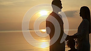 Silhouettes of happy family at amazing sunset. Father, mother and daughter. Dad and mum keep daughter`s hand. slow