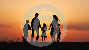 Silhouettes of happy family holding the hands in the meadow during sunset.