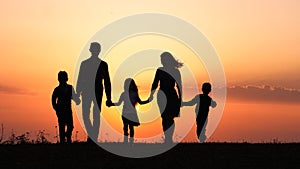 Silhouettes of happy family holding the hands in the meadow during sunset