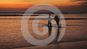 Silhouettes of happy family walking on sea coast during beautiful sunset