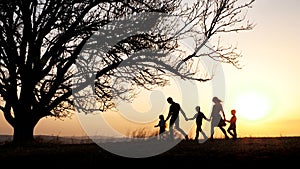 Silhouettes of happy family walking together in the meadow during sunset